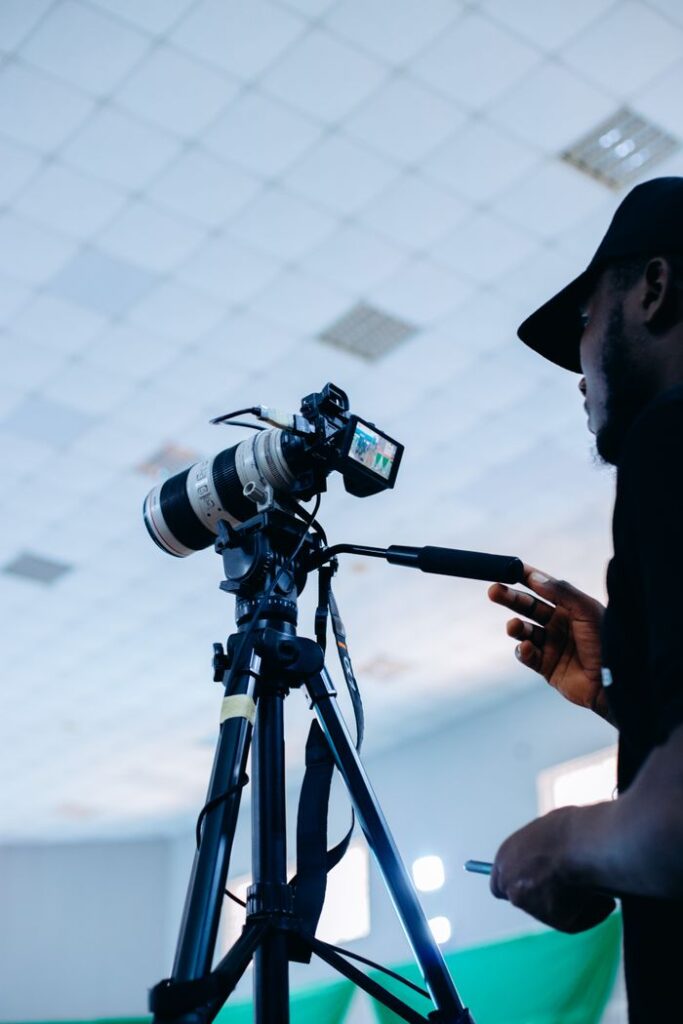 A professional cameraman adjusting a DSLR camera on a tripod inside a well-lit studio.